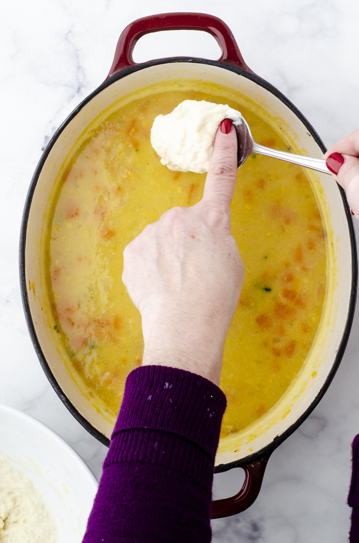 Drop dumplings being dropped onto the top of a pot of potato soup.