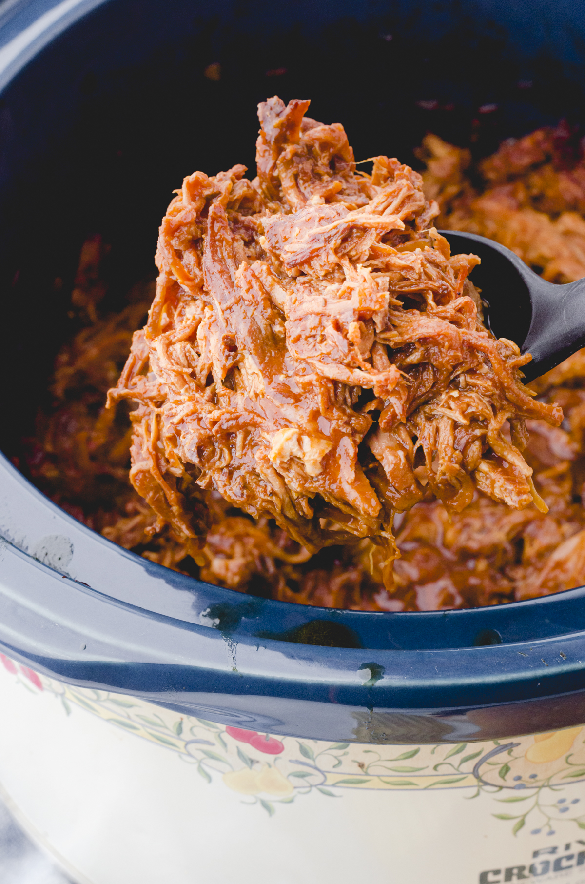 A serving spoon dishing out pulled pork in crock pot