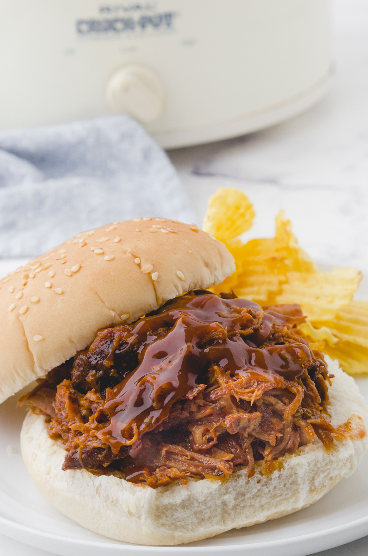 A crock pot pulled pork sandwich with barbecue sauce drizzled on the top of the meat.