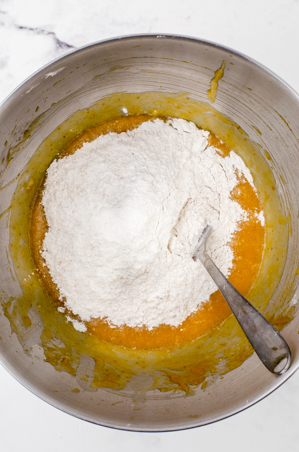 Dry ingredients added into the wet ingredients in the bowl of an electric mixwer and being mixed together with a large spoon for pumpkin banana muffin batter.