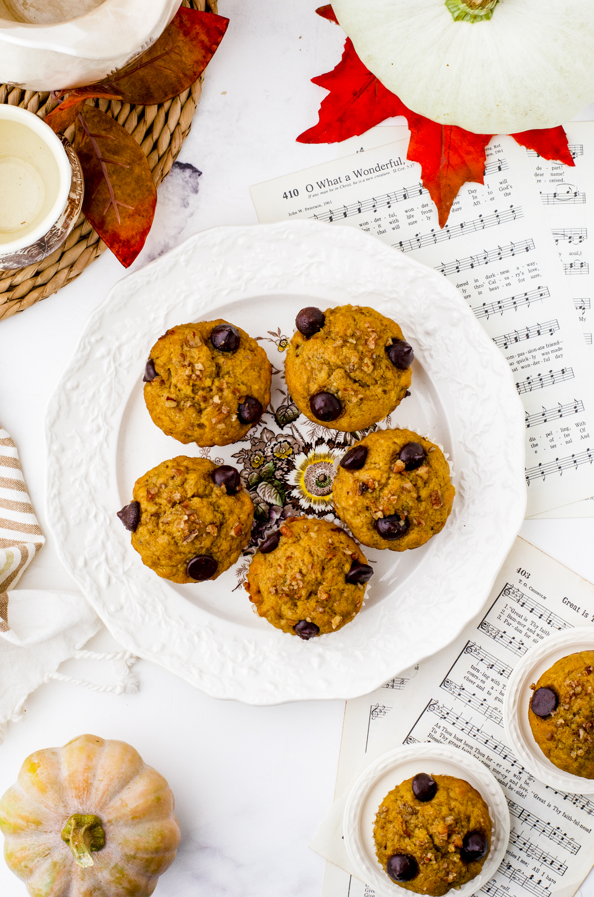 Pumpkin banana Muffins on a serving plate with a mini pumpkin beside it.