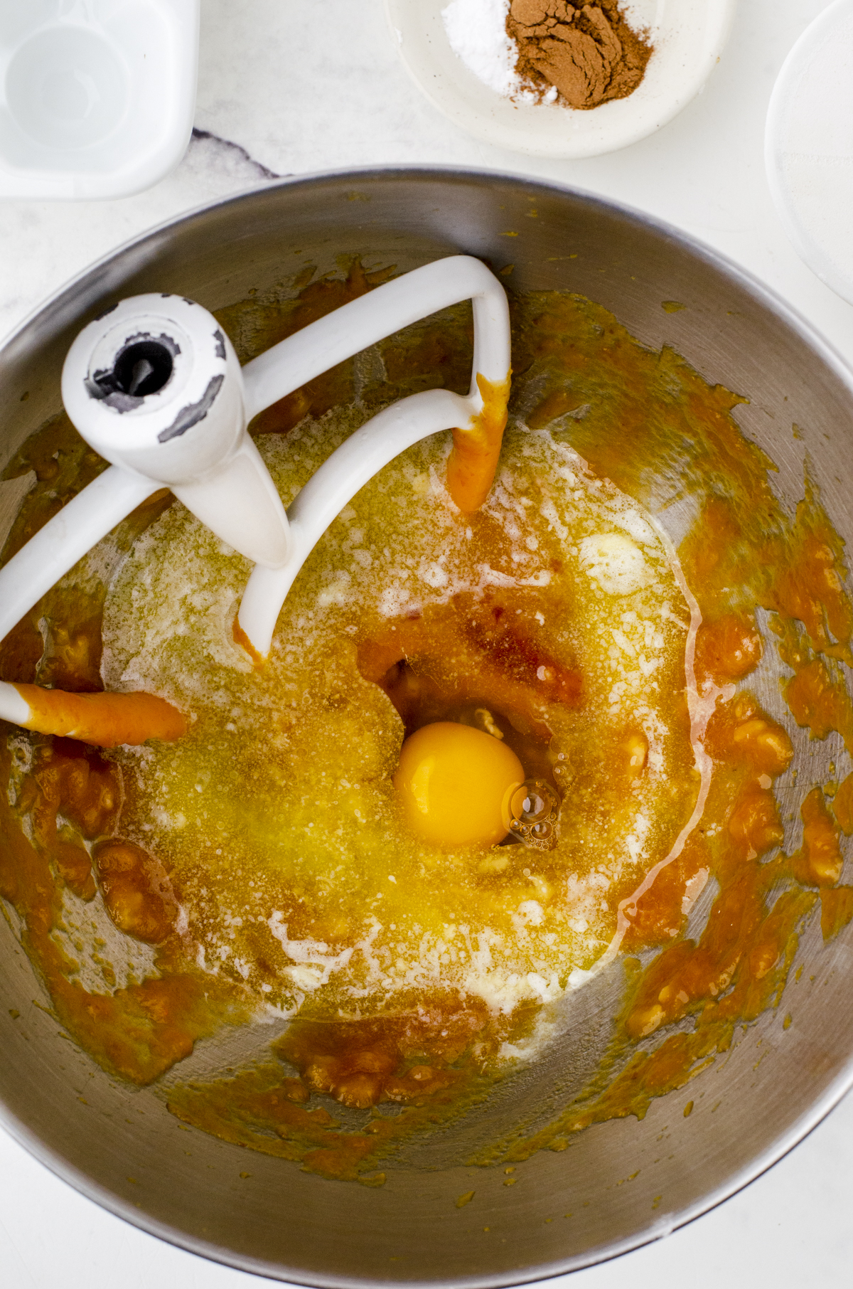 An egg, butter and vanilla that has been added to the pumpkin mixture in the bowl of an electric mixer for banana pumpkin muffins.