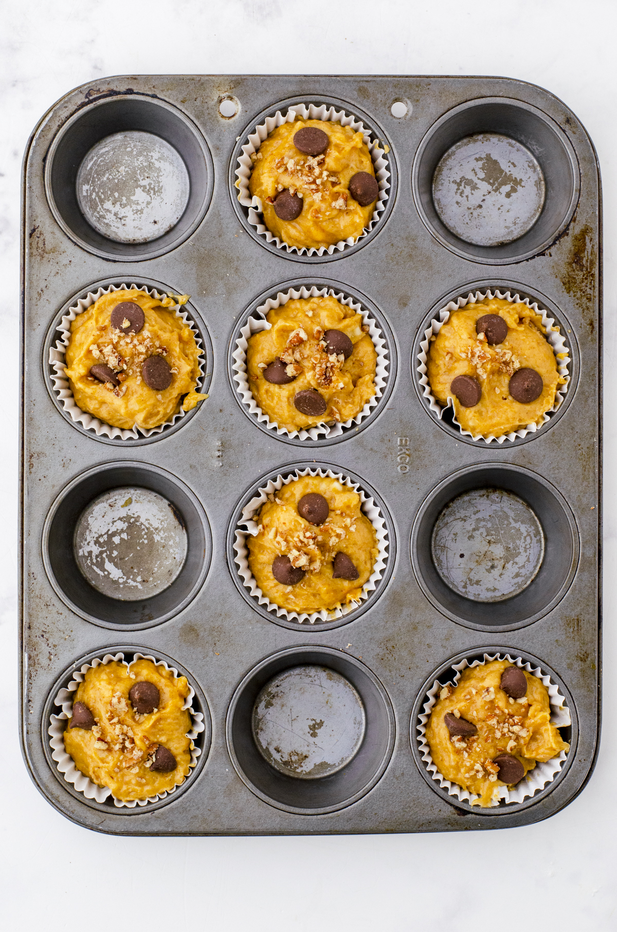 Easy pumpkin banana muffins batter with chocolate chips on the top in a muffin tin.