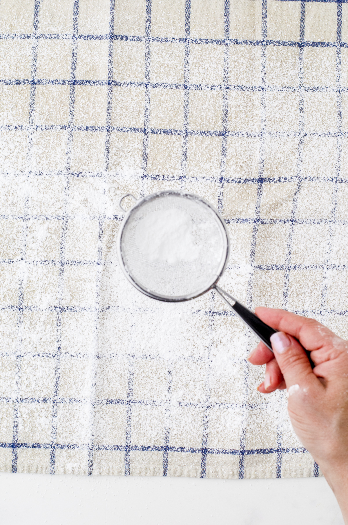 icing sugar being sprinkled onto a tea towel for pumpkin cake roll