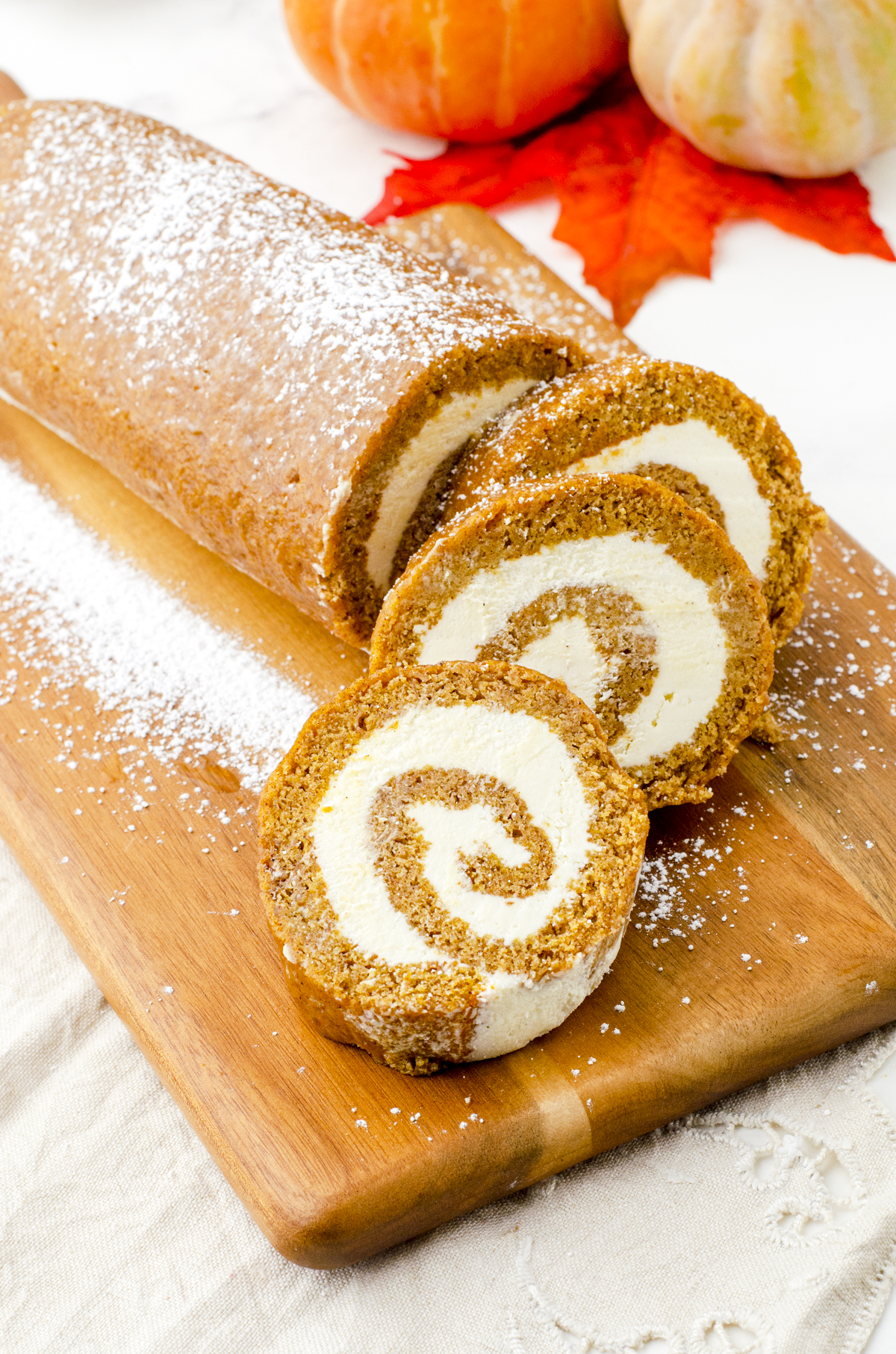 Pumpkin roll cake recipe sliced on a wooden cutting board and sprinkled with icing sugar.