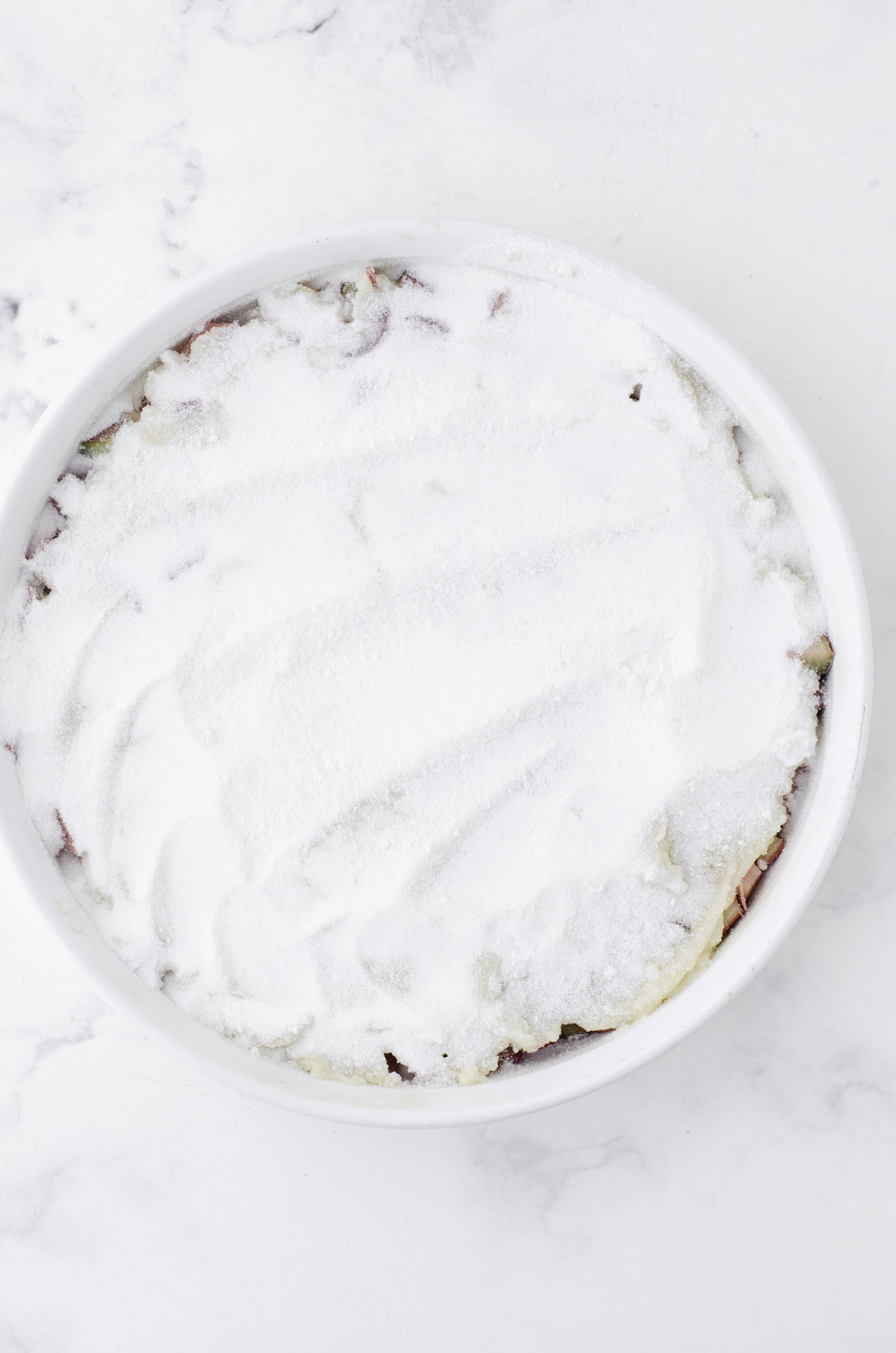 The powdered sugar and cornstarch mixture spread over the cake mixture for sticky rhubarb pudding that is baked in the oven