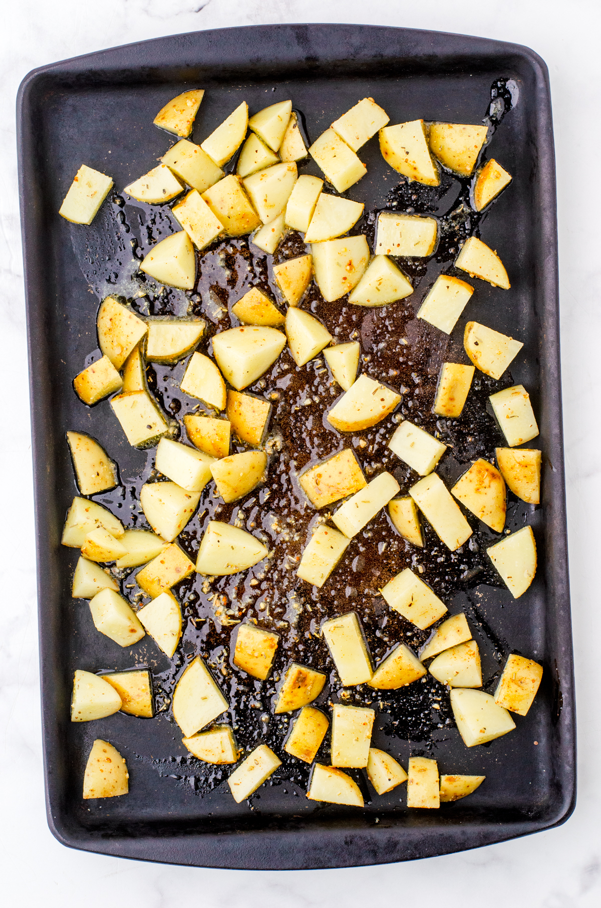 Diced potatoes with olive oil and spices on a stoneware pan ready to be baked