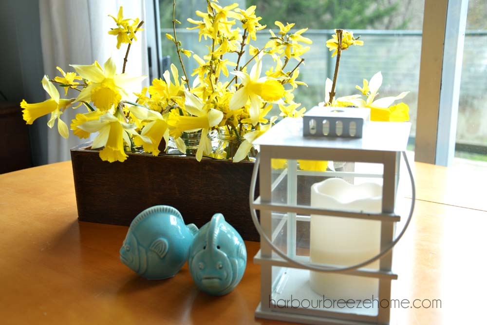 A spring decor arrangment on a tabletop with a daffodil flower arrangment, white lantern, and blue fish salt and pepper shakers