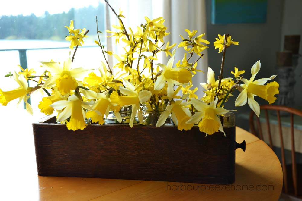 daffodil flower arrangements placed in an antique sewing machine drawer sitting on a table top