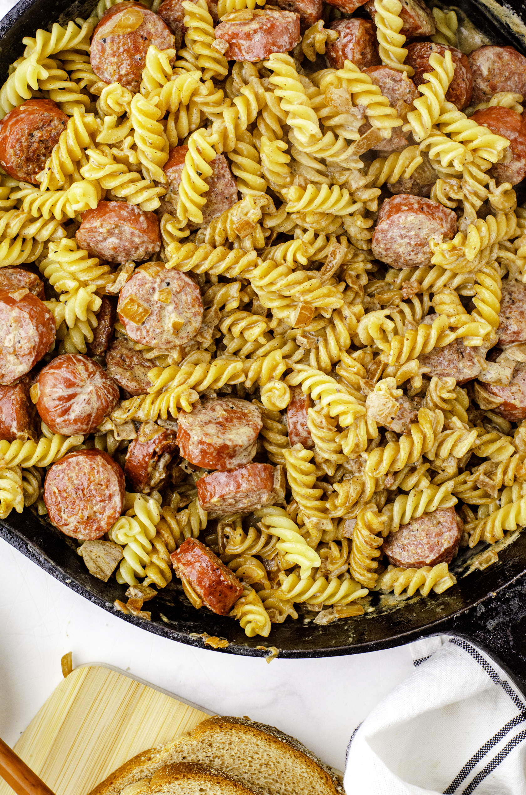 Mennonite sausage, cooked pasta noodles, and cream gravy mixed together in a cast iron skillet for Mennonite sausage and cream gravy skillet dinner.