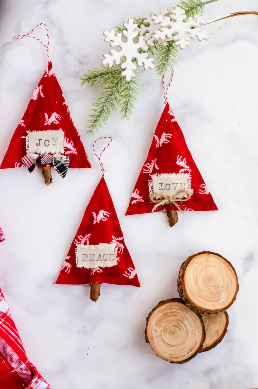 3 Red and White DIY Scandinavian Christmas ornaments made out of fabric and stamped with the words "joy, love, and peace".