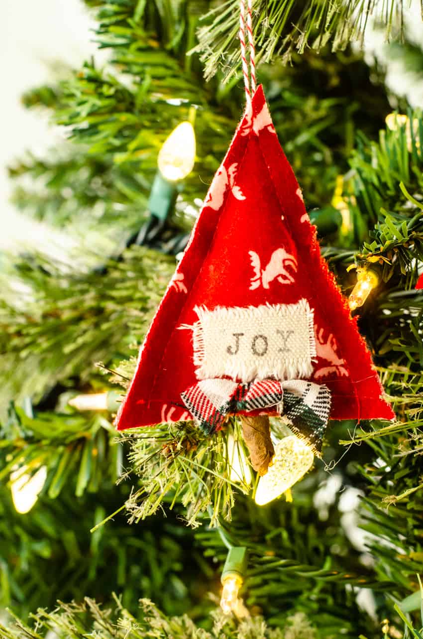 DIY Scandinavian fabric Christmas Ornament shaped like a tree with the word "joy" on it hanging in a tree.