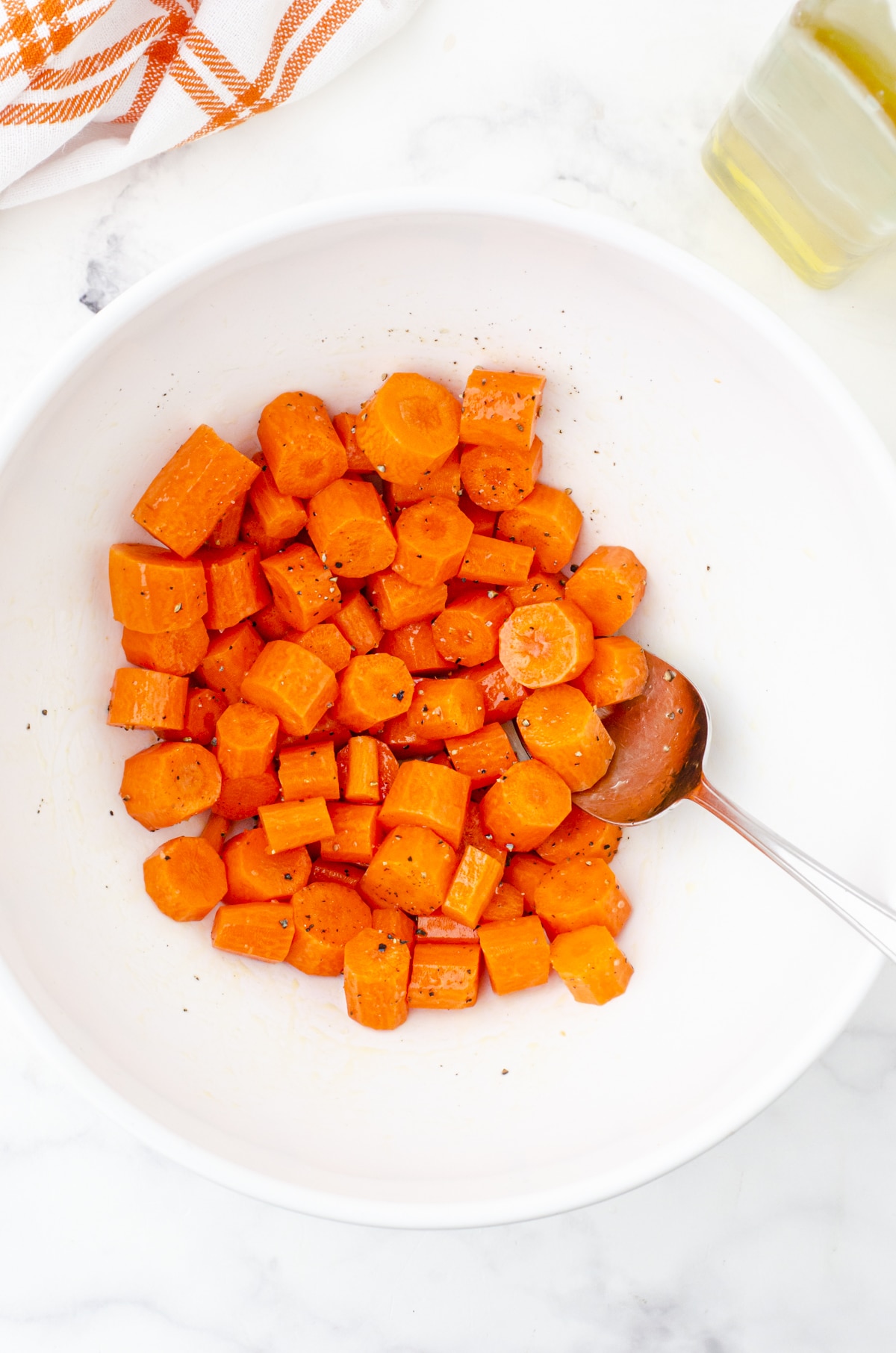 Carrots in a medium sized bowl being tossed with olive oil for sheet pan chicken and veggies recipe.