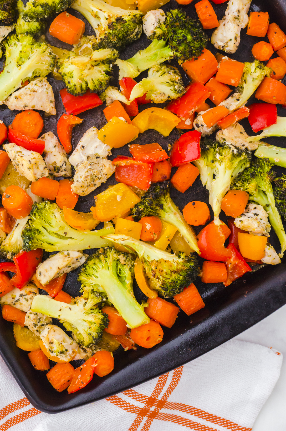 Close up of sheet pan chicken and veggies ingredients in a sheet pan - chicken, brocolli, peppers, and carrots.