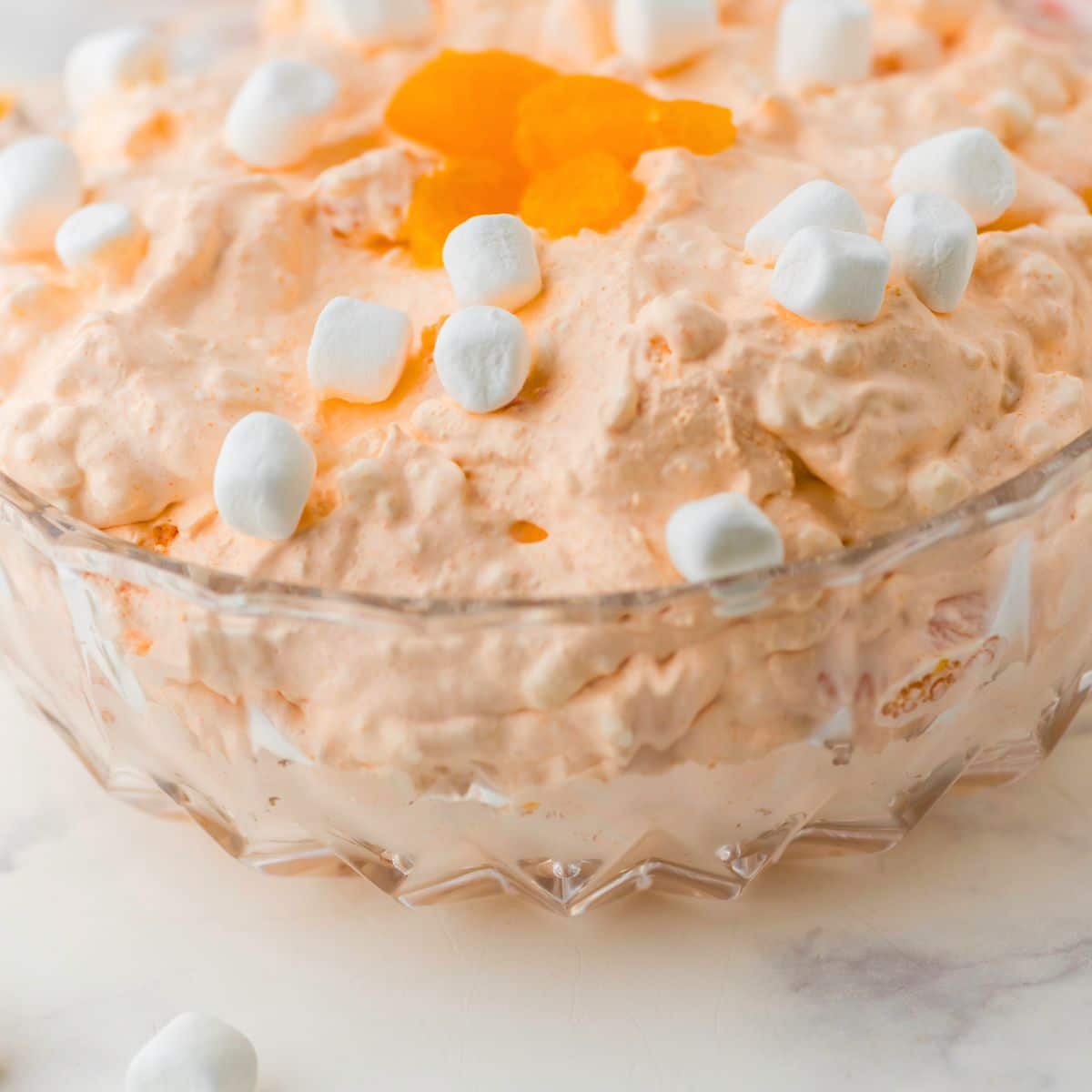 orange fluff salad in a clear glass serving bowl
