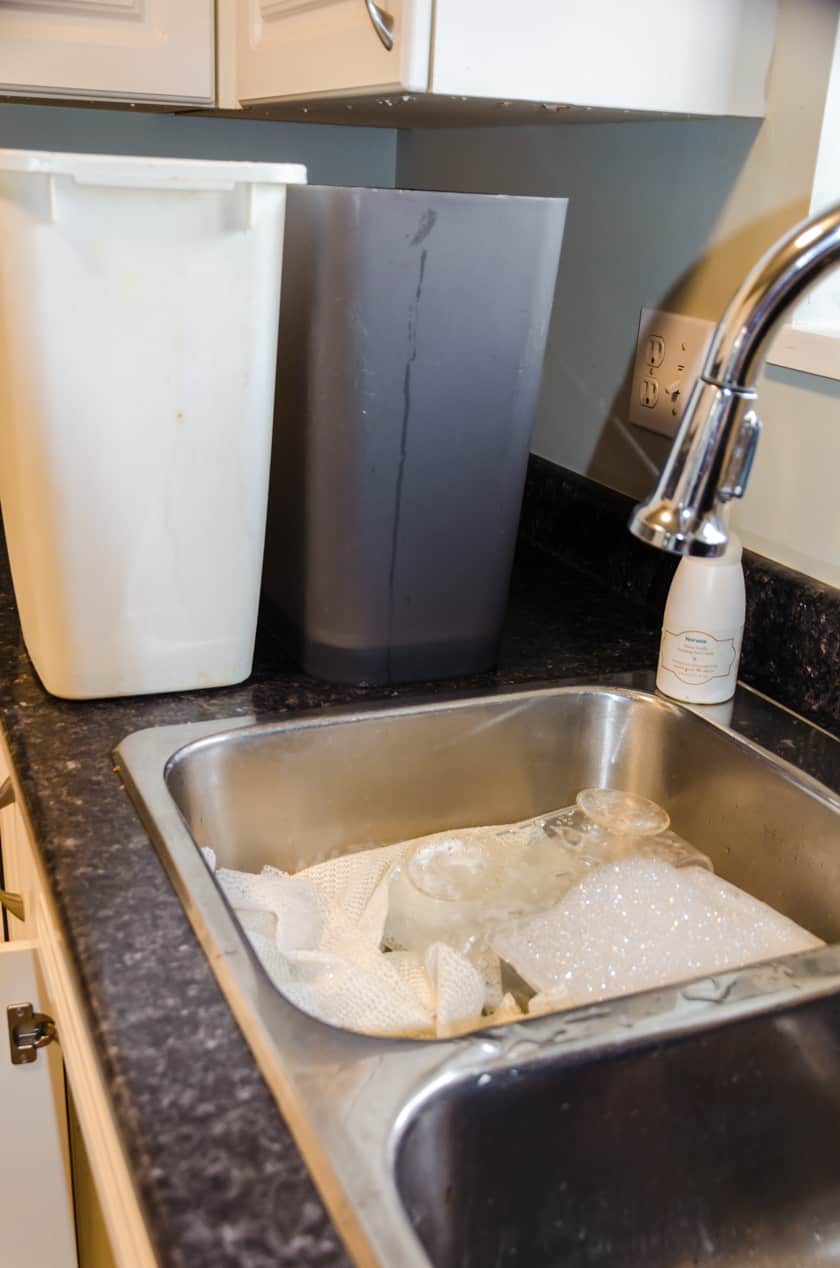 Garbage cans soaking in water and a sink full of soapy water with organizational containers in it.