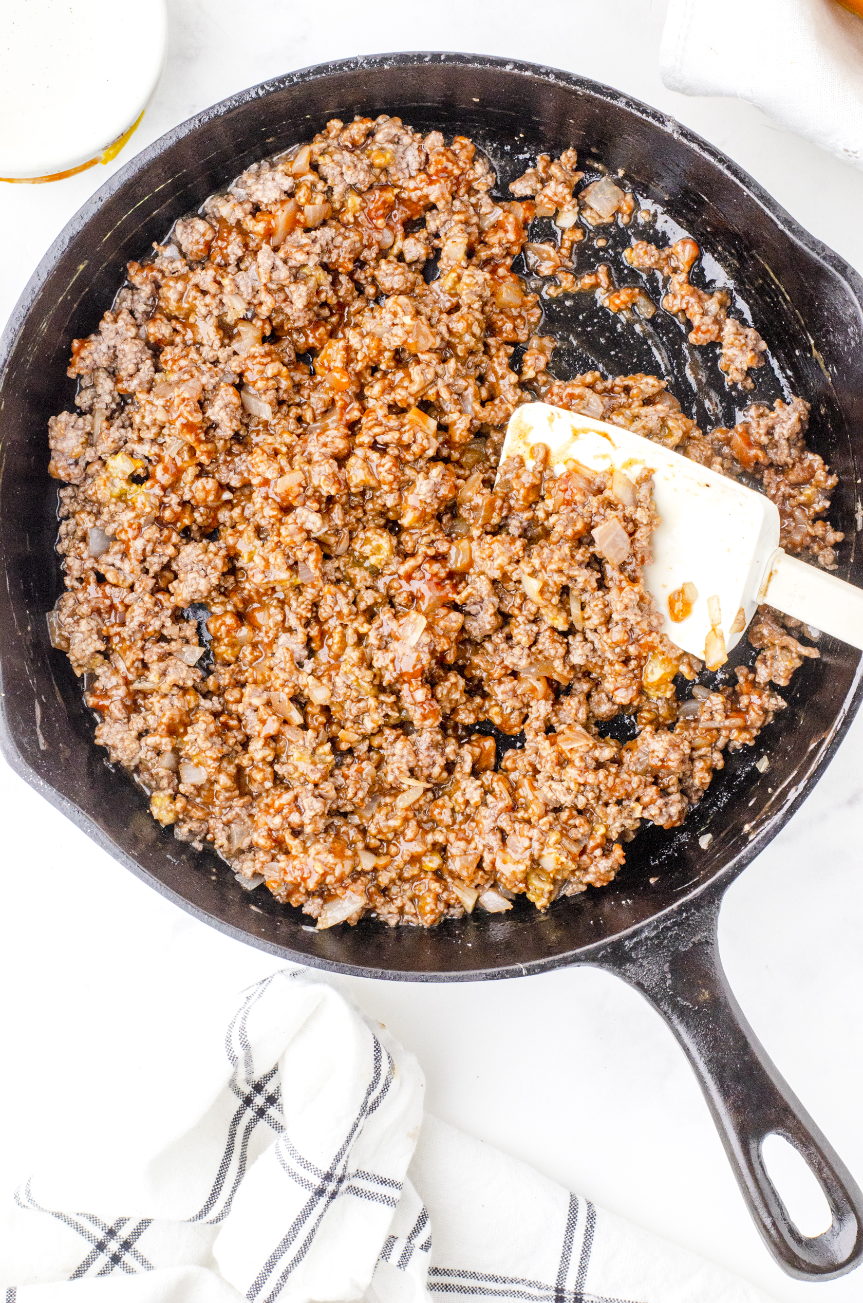 Sloppy joe sauce stirred into browned hamburger and onion in a cast iron skillet.