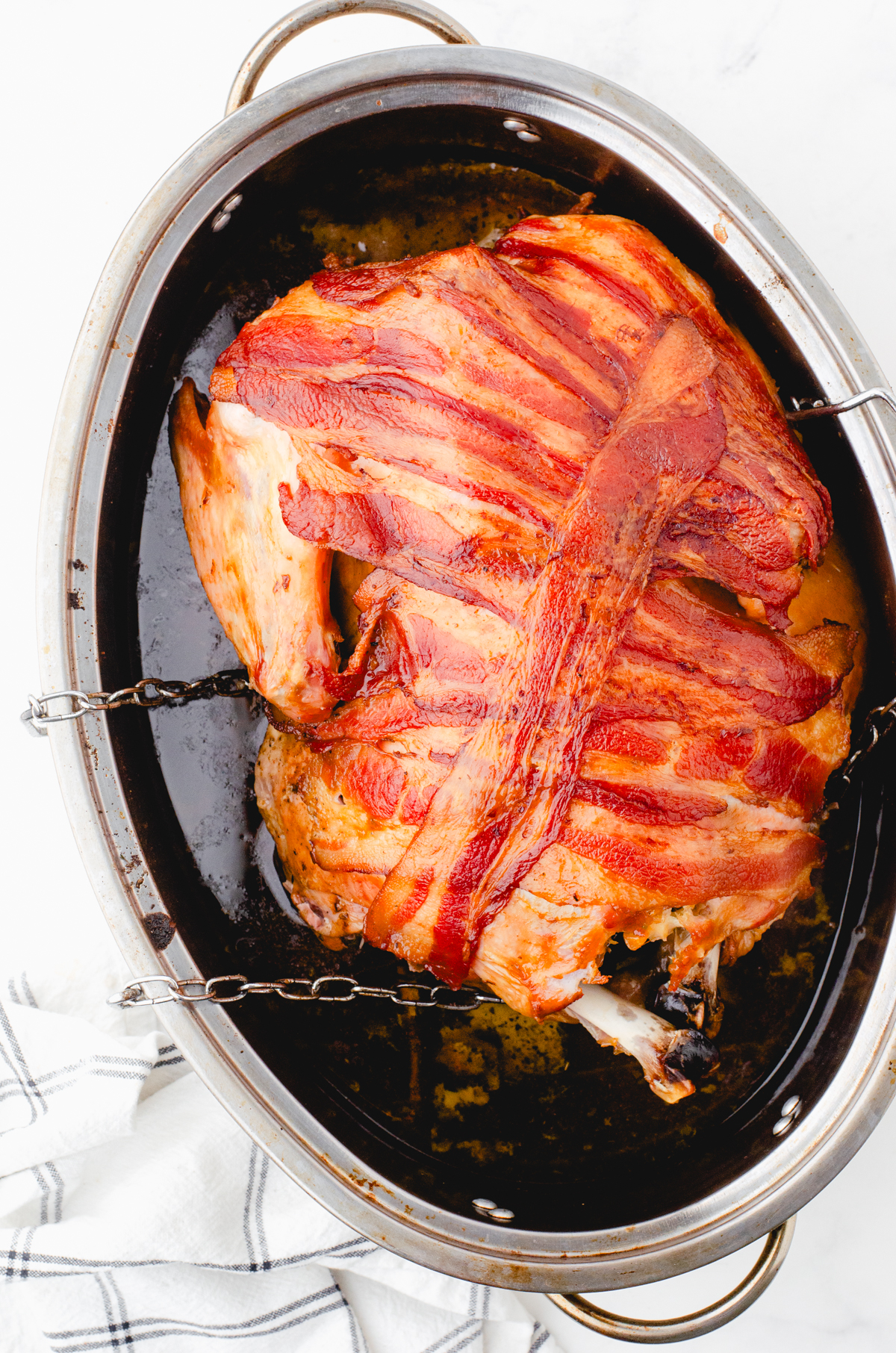 Roasted whole turkey with crispy bacon covering it in a roasting pan.