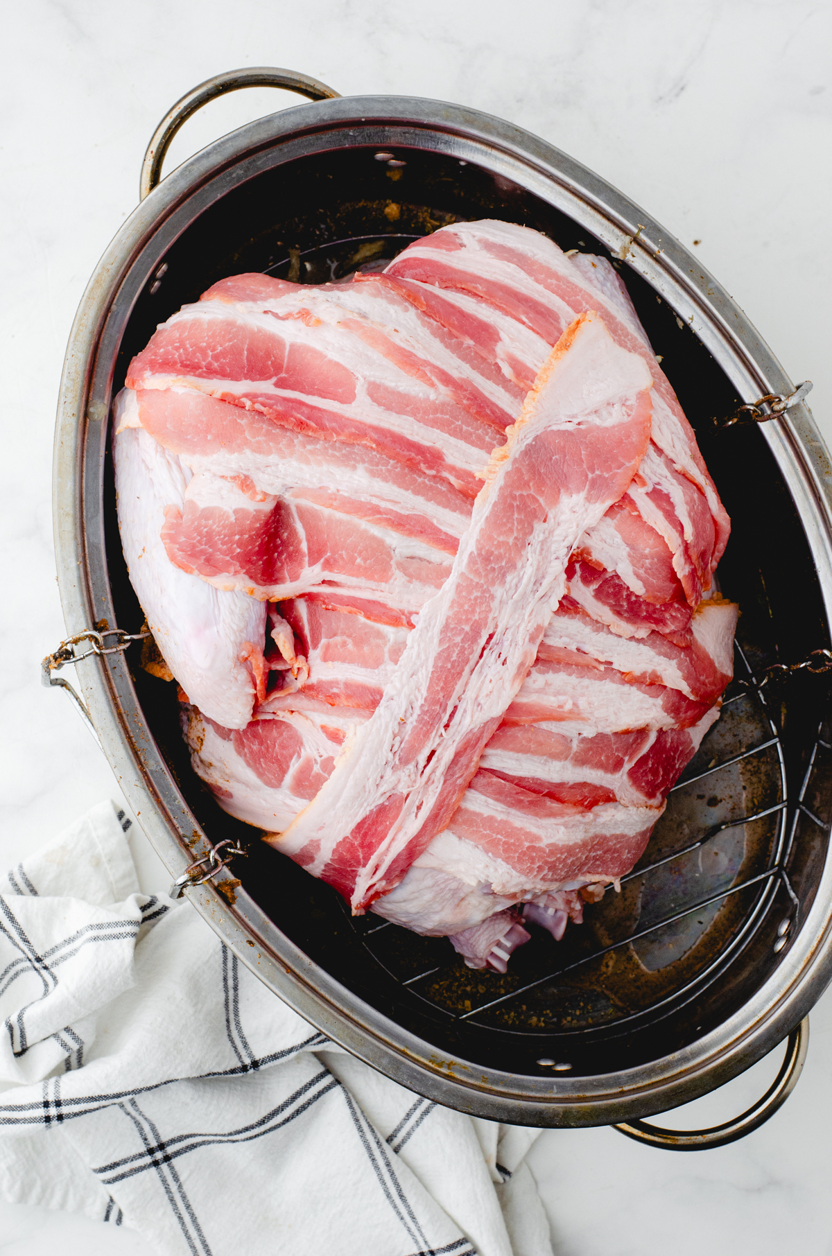 Whole turkey in roasting pan covered with strips of bacon
