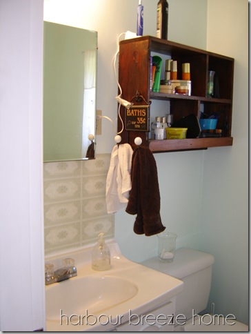 Small Bathroom Vanity area with small vanity, built in medicine cabinet mirror, and a dark wood rustic shelf above the toilet.