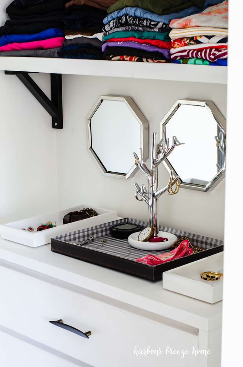 Jewelry in trays on top of a dresser in a small closet.