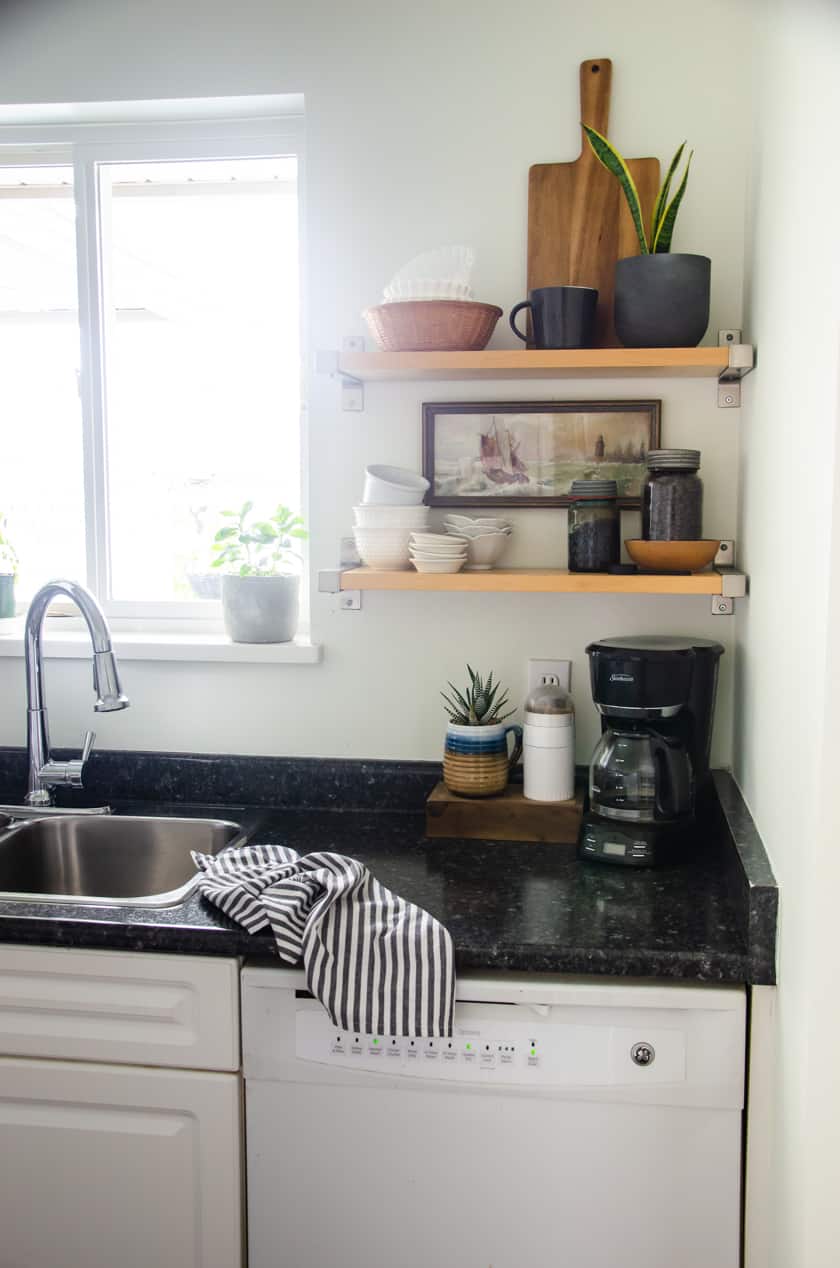Open shelves with a snake plant, wooden cutting board, antique art print, and bowls as decor.