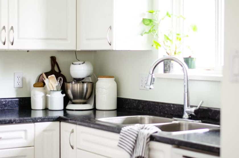 A mixer and canisters sitting on the counter of a small kitchen in the corner beside the sink.