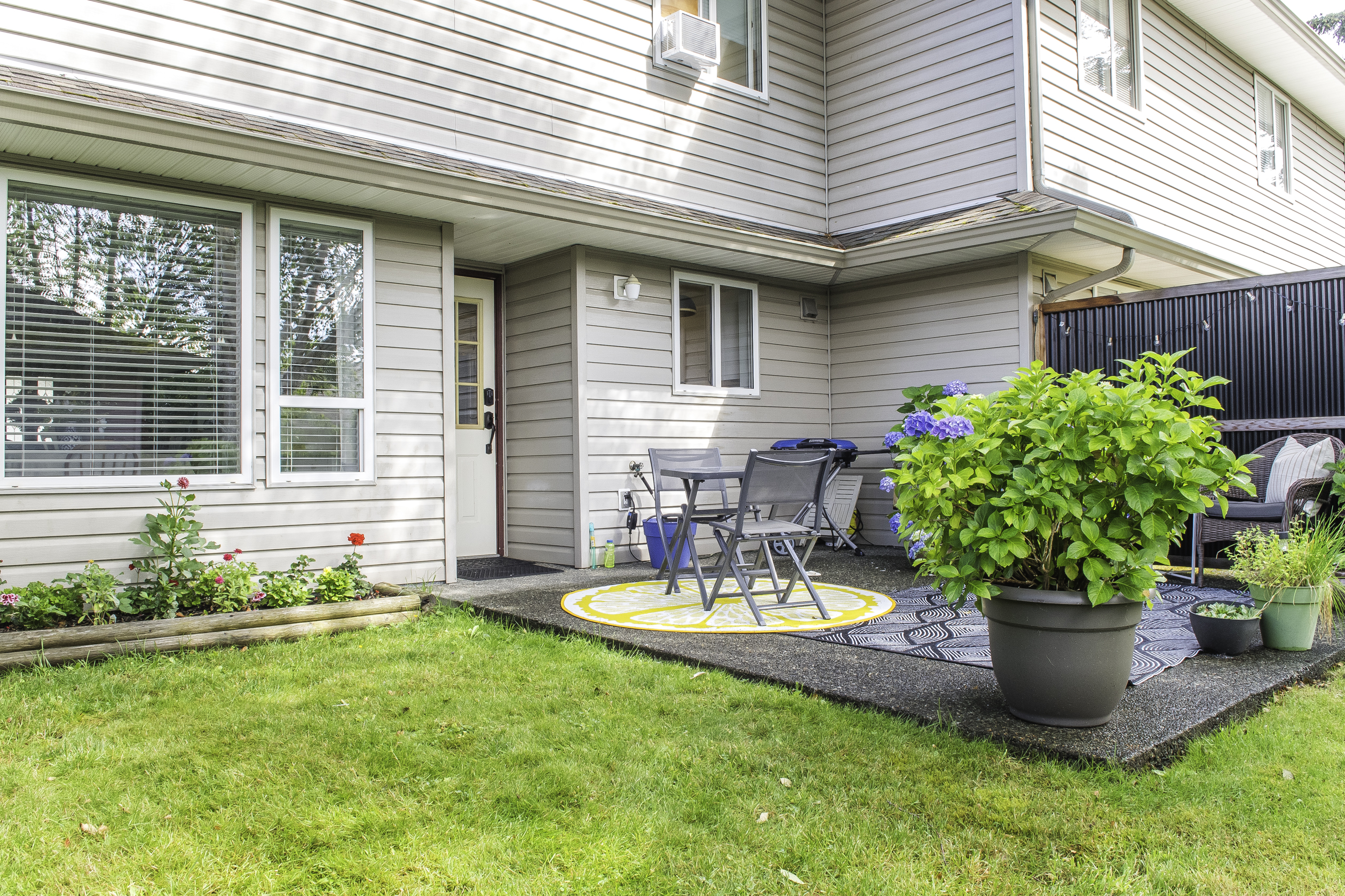 A small concrete slap patio outside a townhouse with a flower bed on one side.