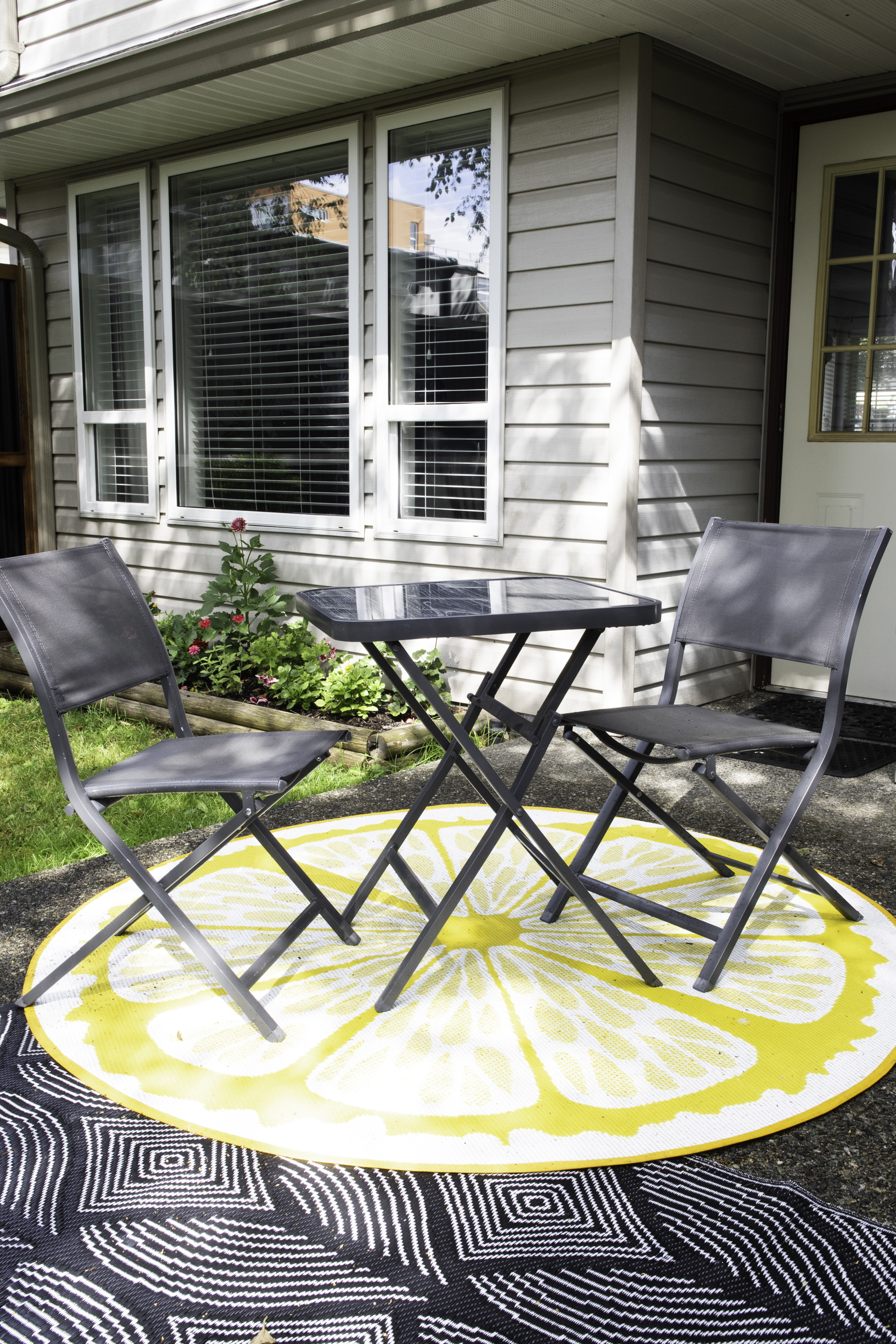 A 3 piece bistro table set sitting on a round outdoor rug.
