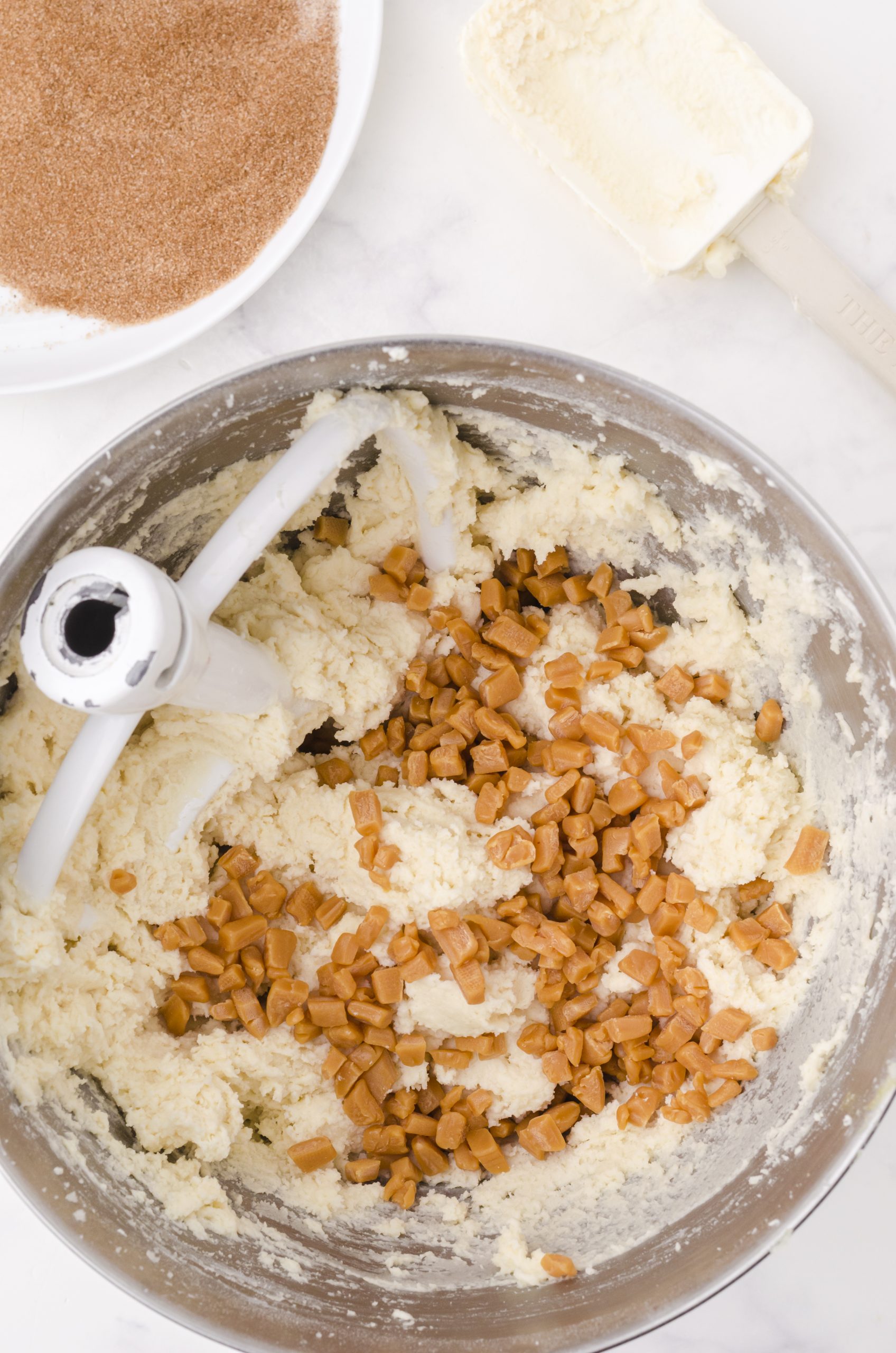 caramel bits added into snickerdoodle cookie dough batter in a bowl