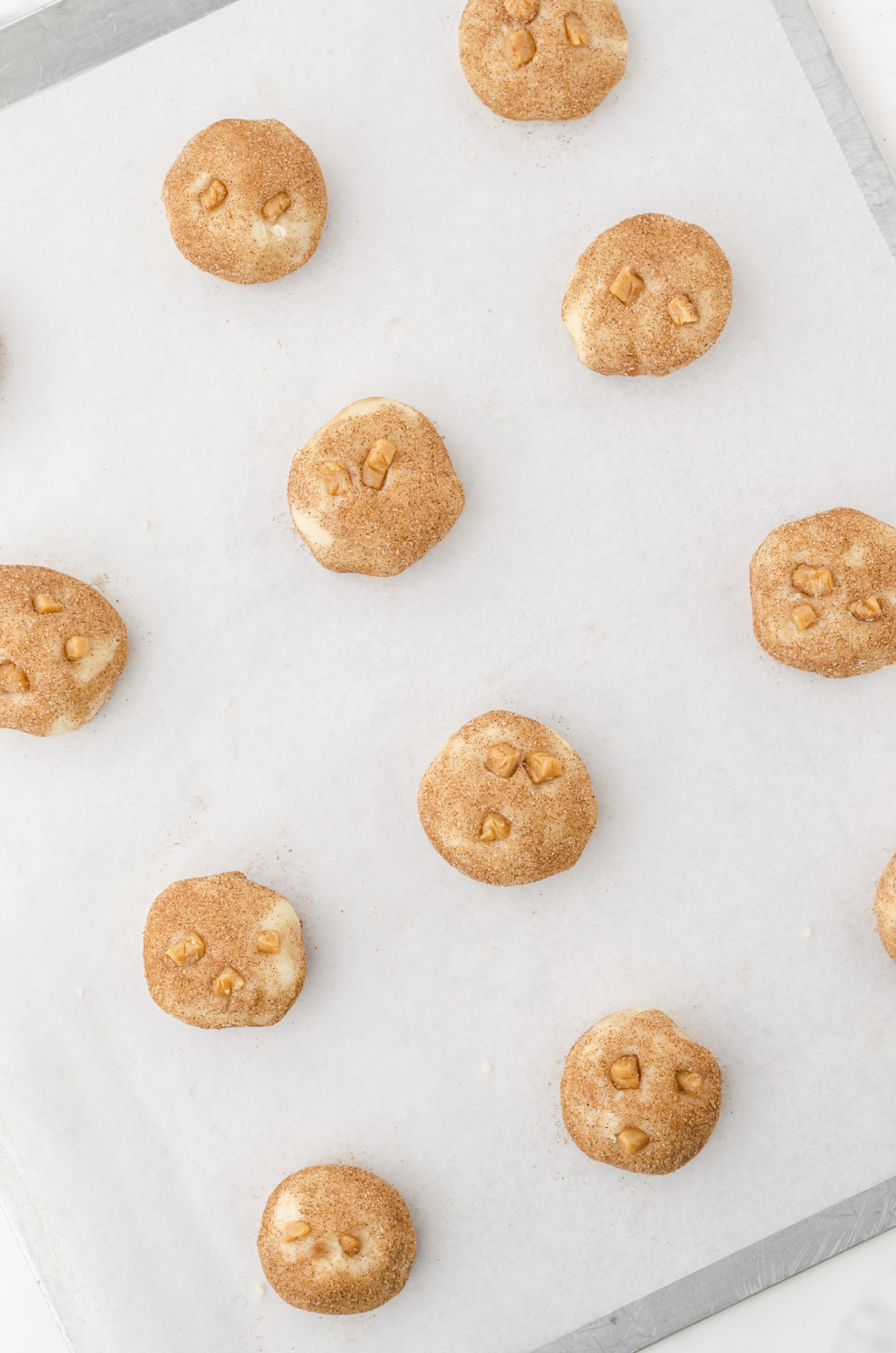 snickerdoodle cookie dough balls on a cookie sheet with caramel bits in the tops