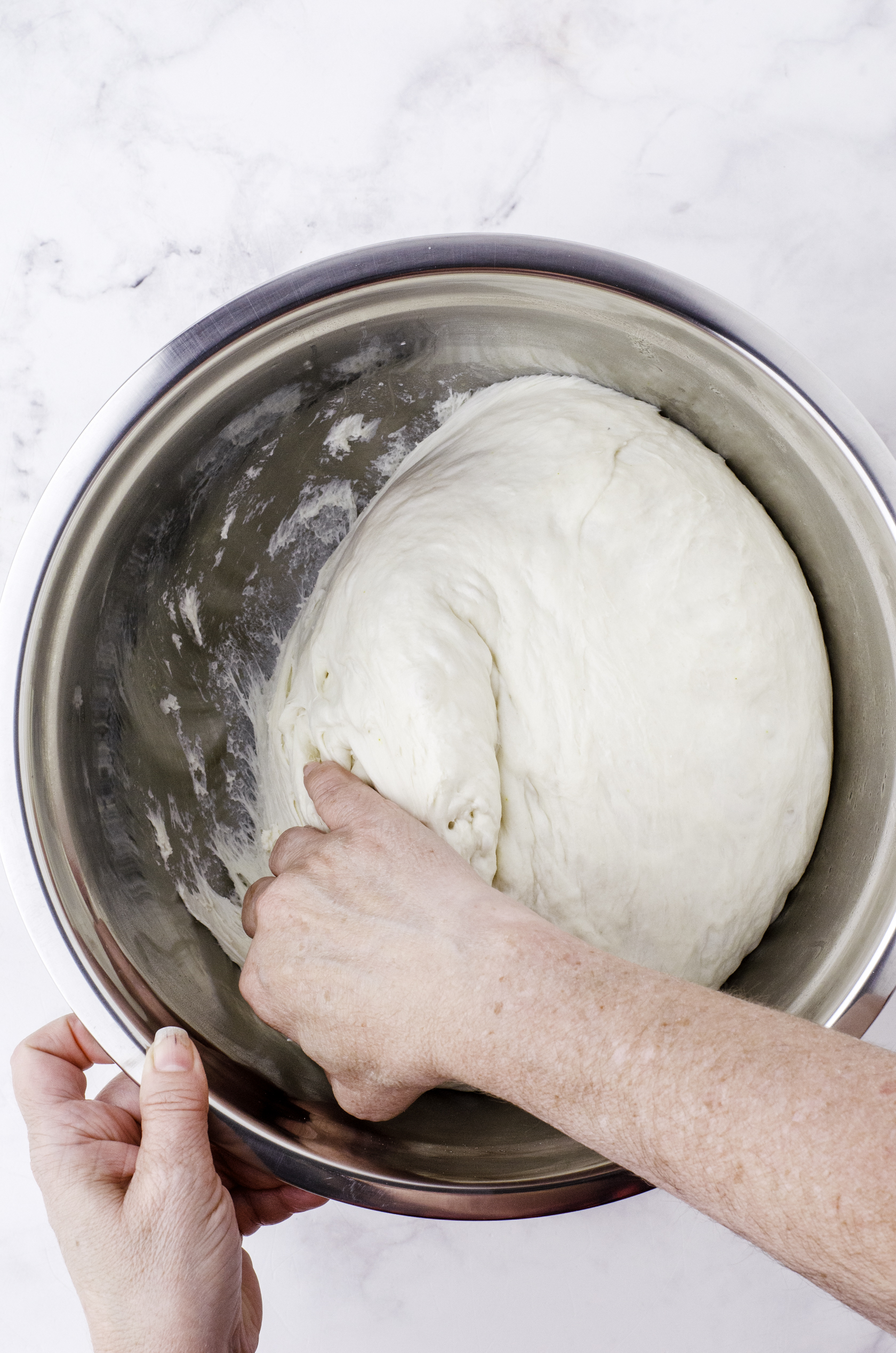A woman pulling the sourdough dough away from the sides of the bowl.