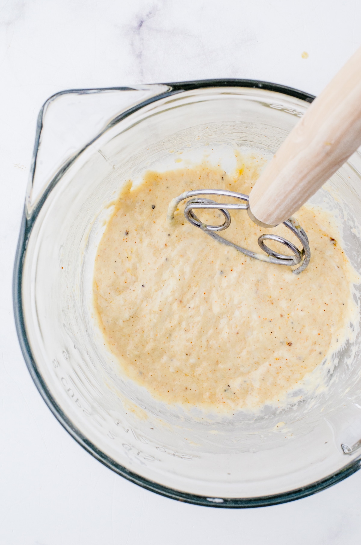 Sourdough discard mixed with spices and oil in a mixing bowl with a danish whisk in it.