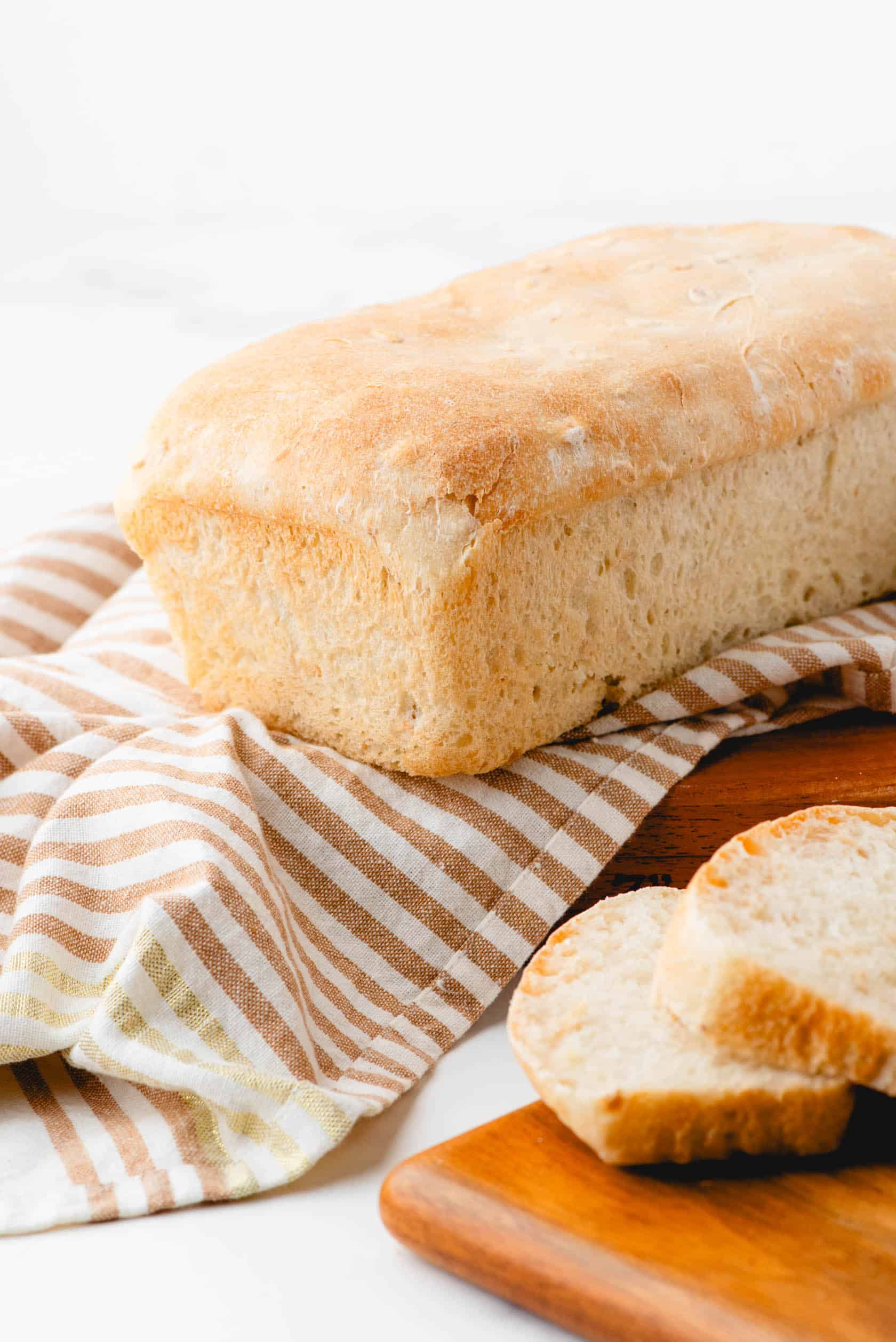 A loaf of honey oat sourdough sandwich bread sitting on a striped cloth with a few slices beside it.