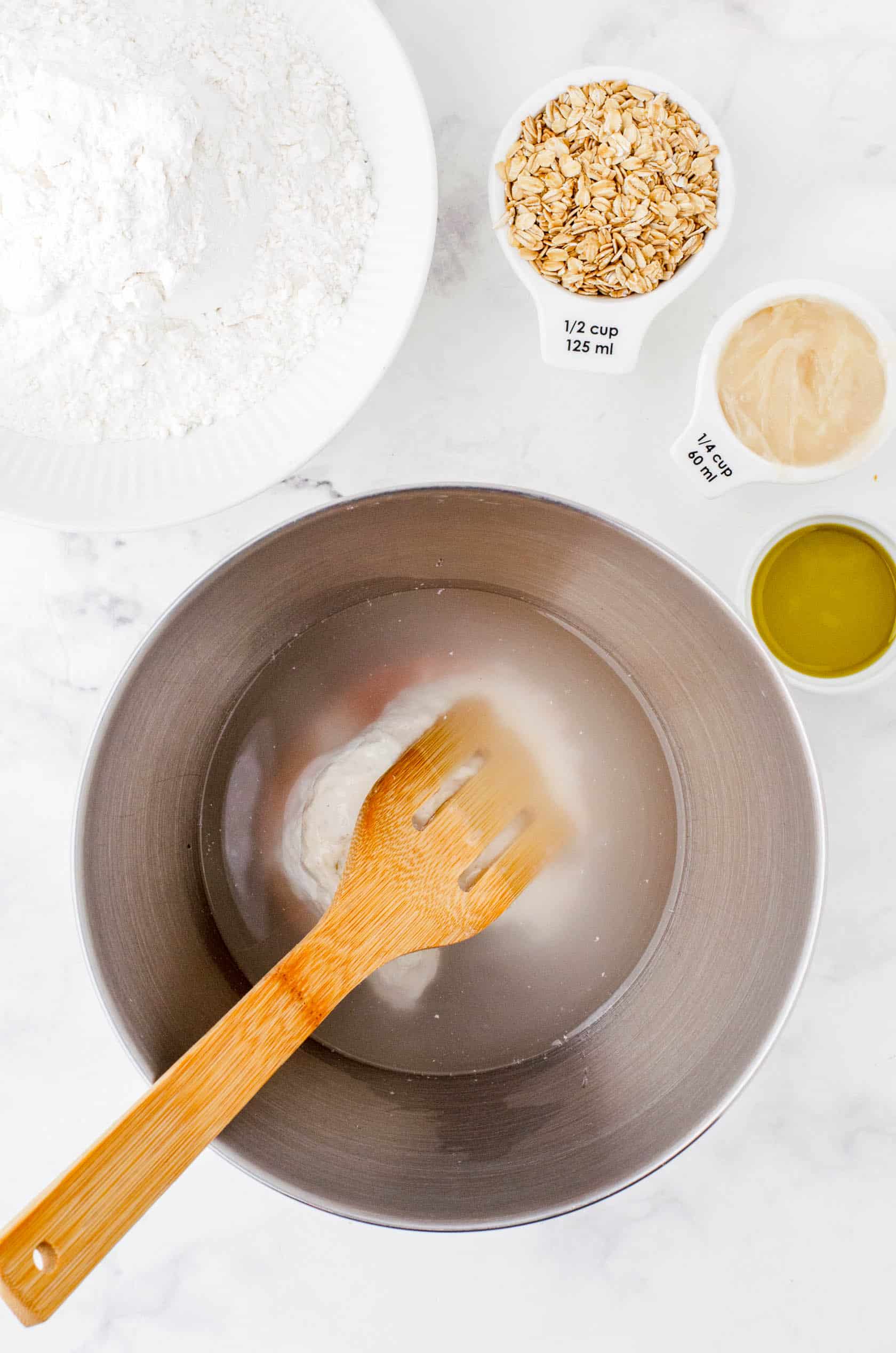 Water, sourdough starter, and salt in the bowl of an electric mixer ready to be stirred.
