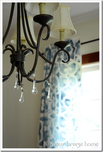 Black chandelier with white lampshades with a glimpse of blue stenciled curtains hanging in the background