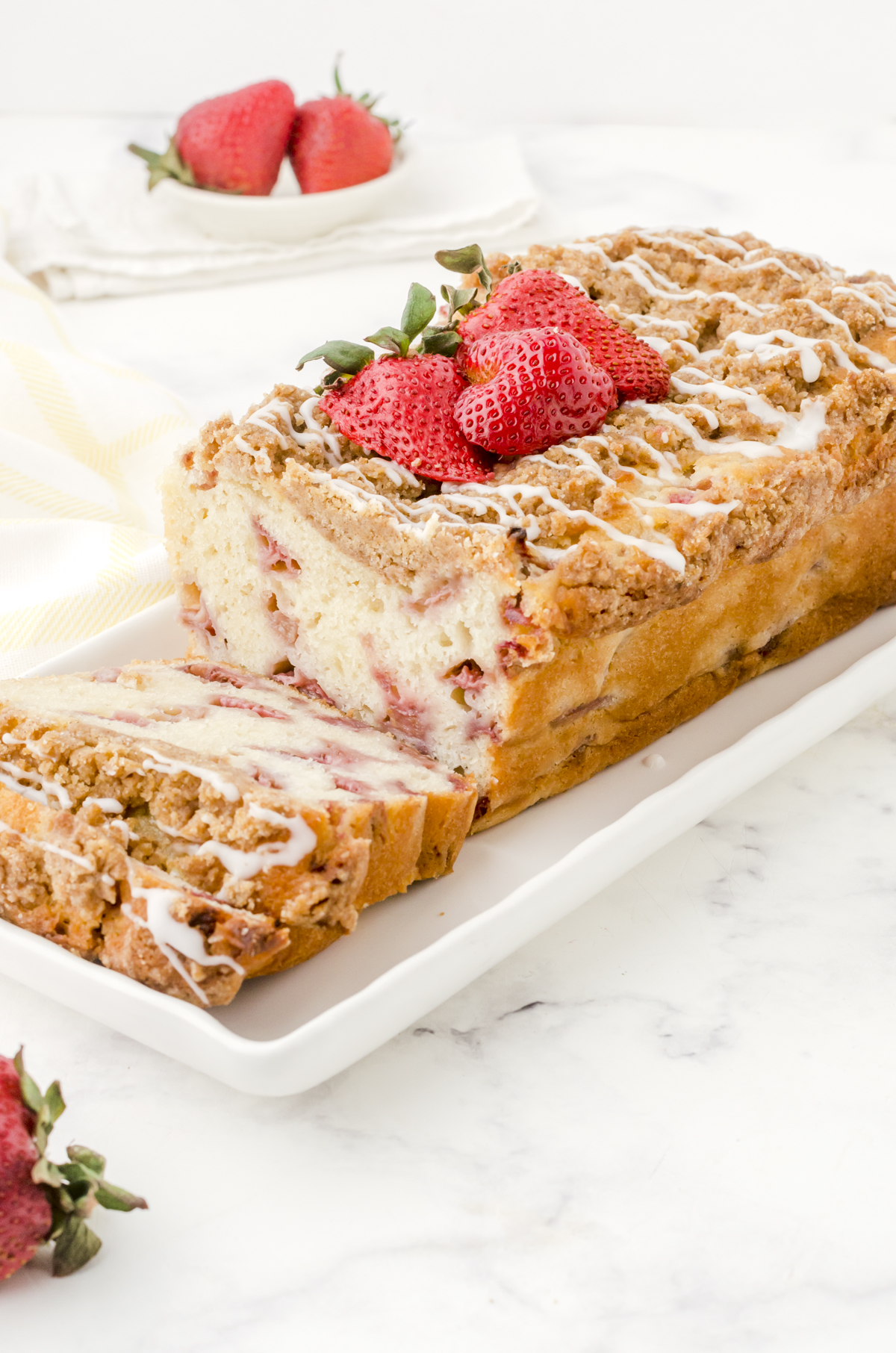 Strawberry bread with crumble topping and vanilla glaze on a white serving platter.