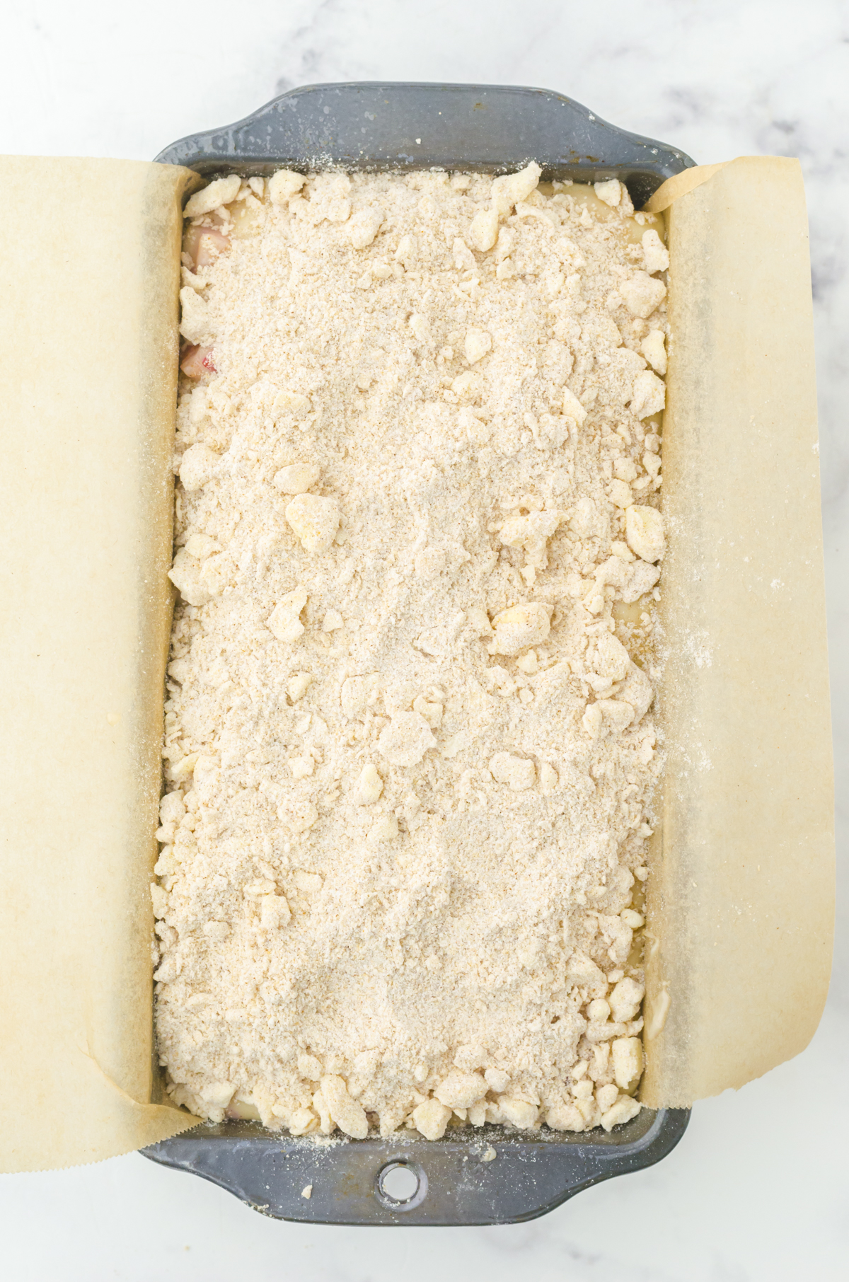 crumble topping sprinkled onto strawberry quick bread batter in a loaf pan lined with parchment paper.