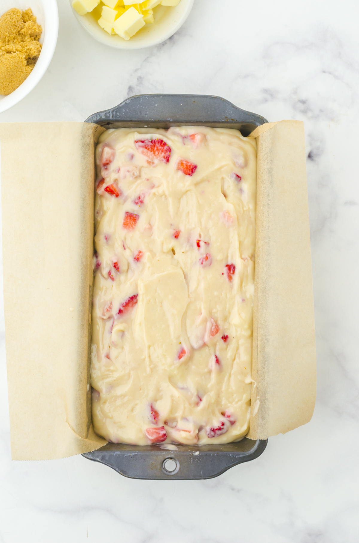 A loaf pan lined with parchment paper filled with strawberry quick bread batter.
