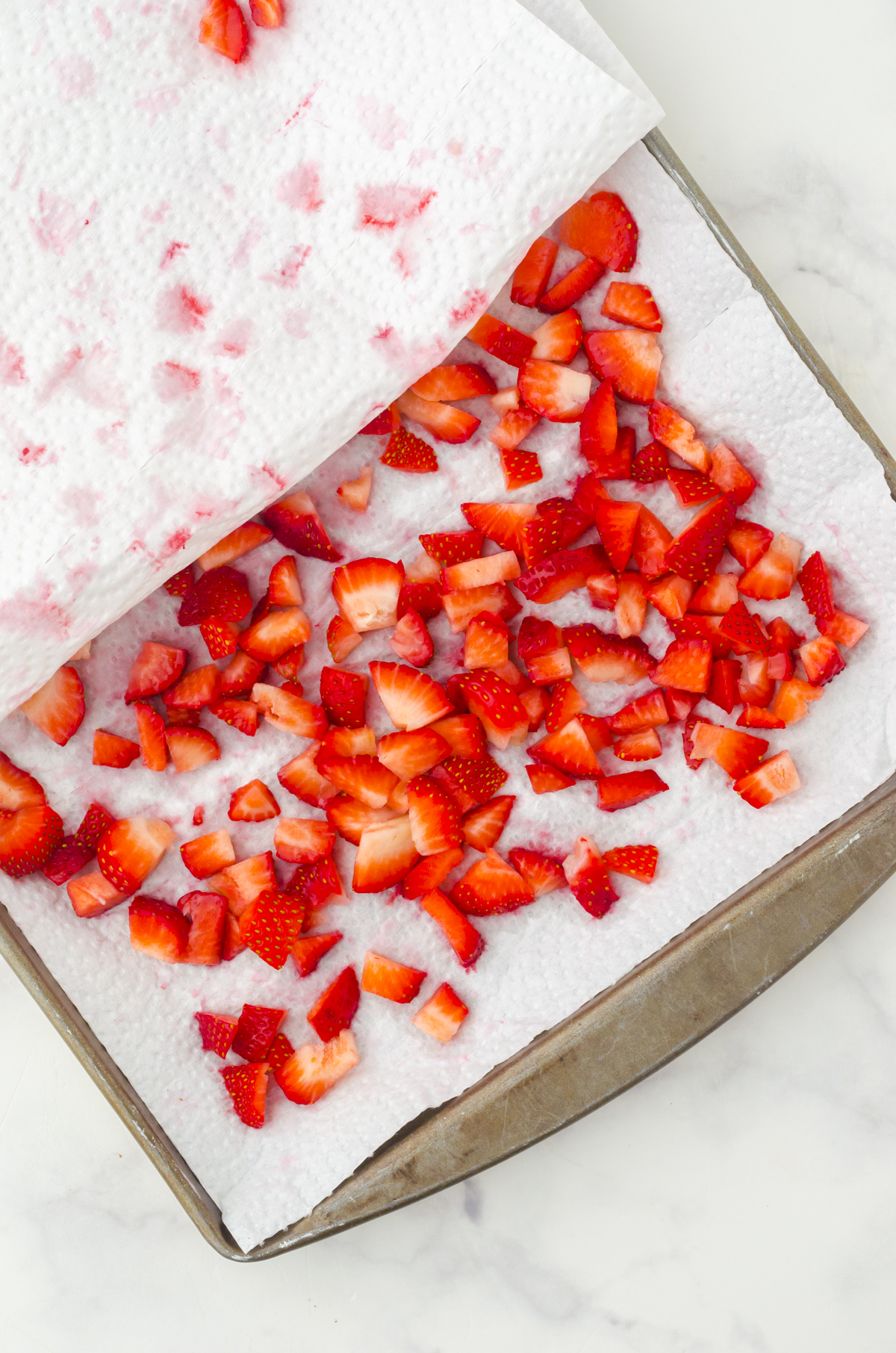 Cut up strawberries sitting on a paper towel in a large baking sheet