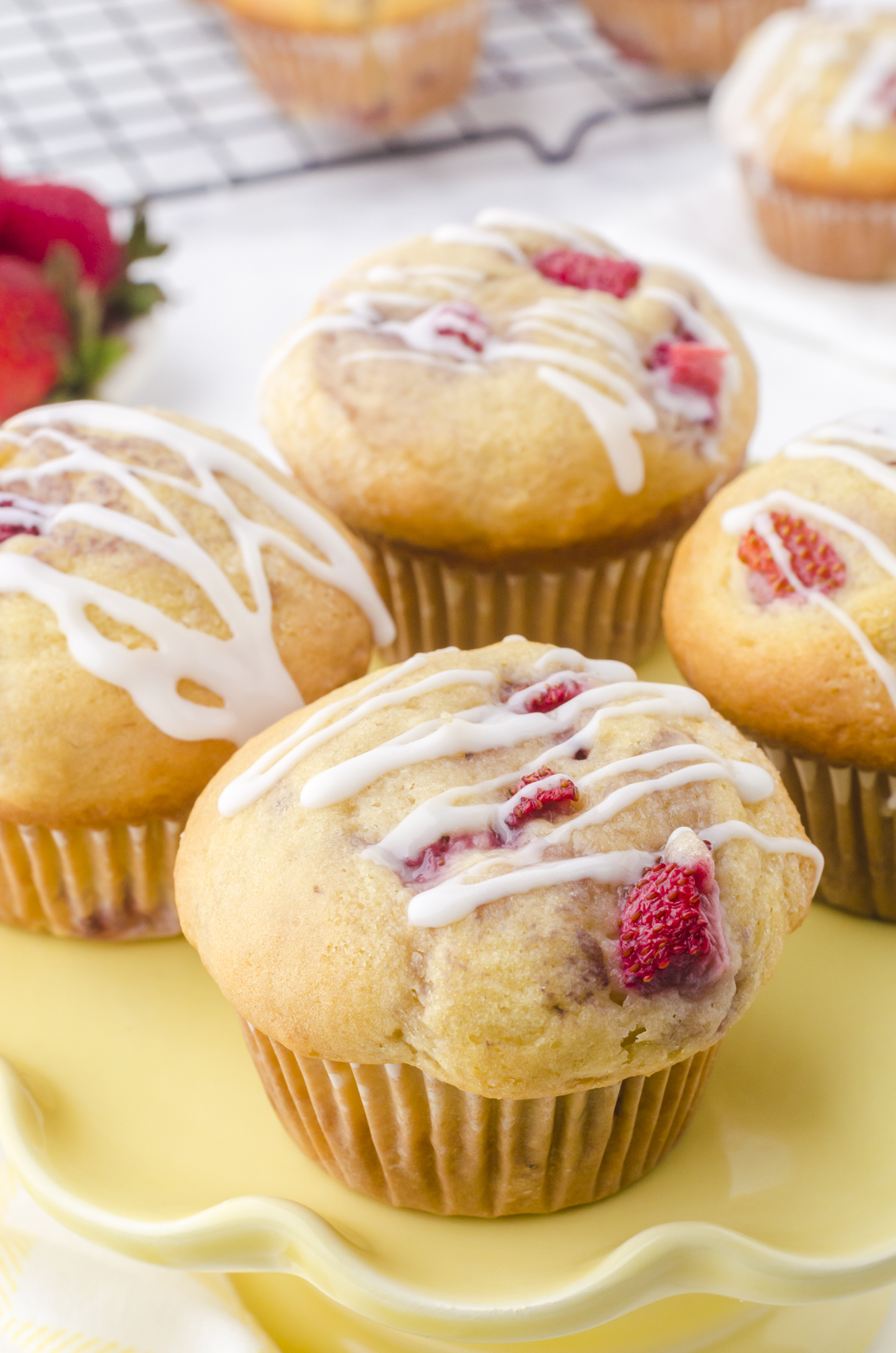Buttermilk strawberry muffins on a yellow serving dish with vanilla glaze drizzled on the tops.