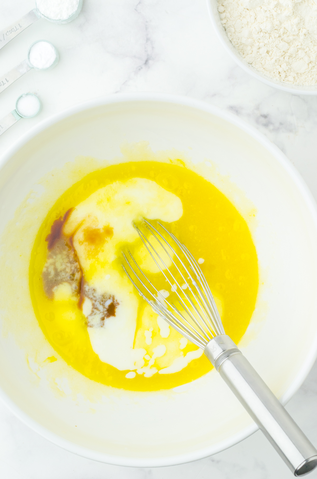 Wisking the wet ingredients for strawberry buttermilk muffins in a white bowl