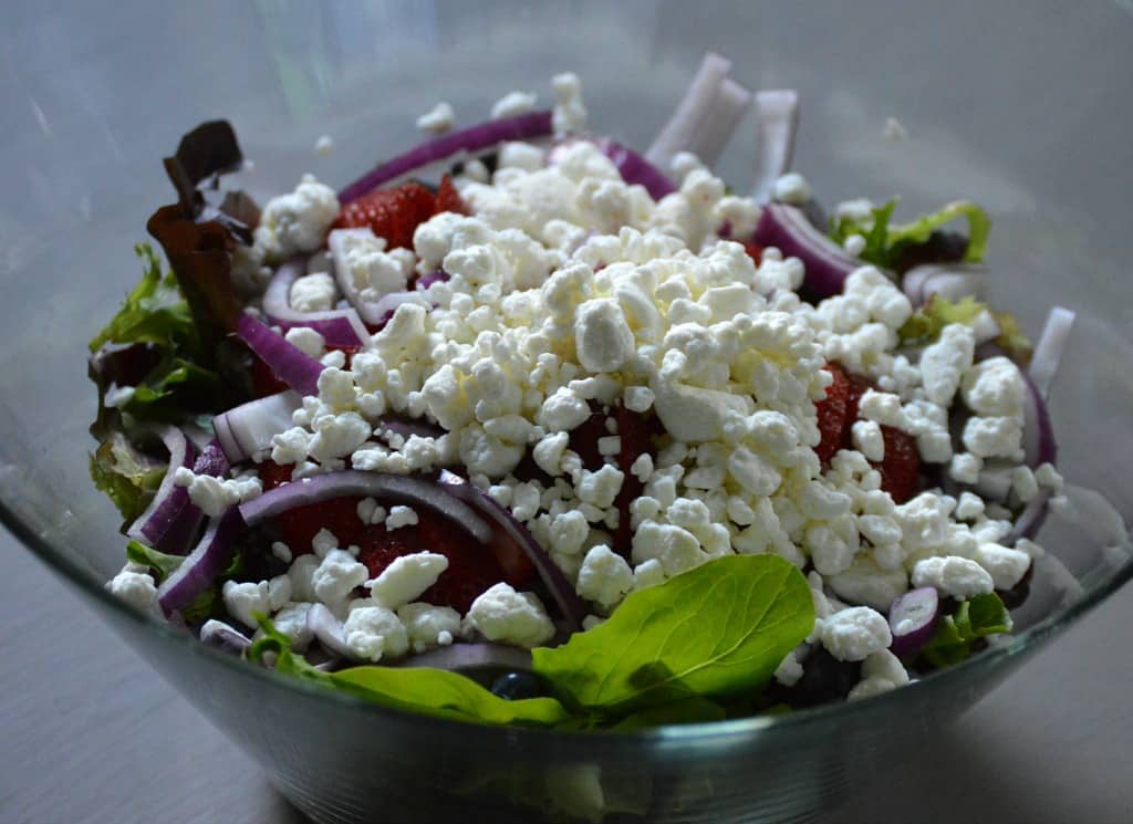Salad greens with white cheese crumbled on the top in a clear glass serving bowl