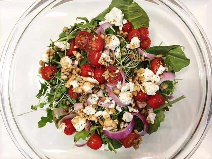 Salad greens garnished with crumbled white cheese, nuts, tomatoes and onions on a clear glass plate
