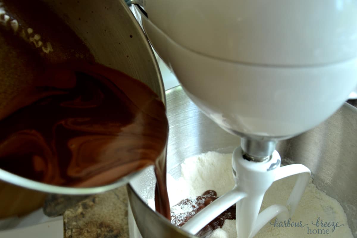 pouring hot ingredients into a mixing bowl with flour to make texas sheet cake brownie batter