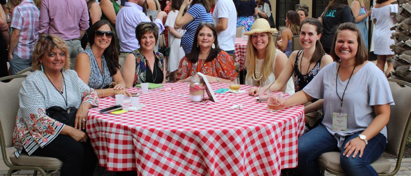 7 women sitting at an outdoor table with red checked tablecloth