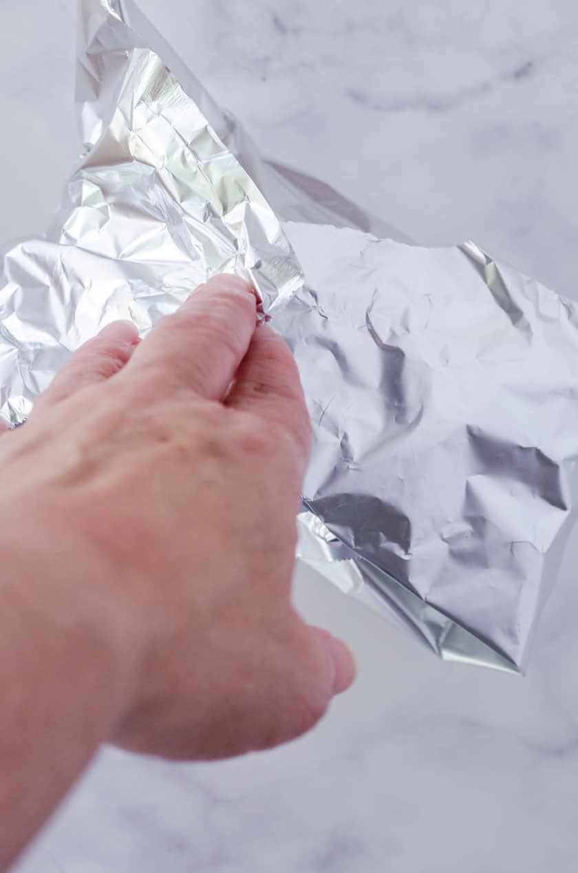 a tuna melt in the oven sandwich being wrapped in aluminum foil.