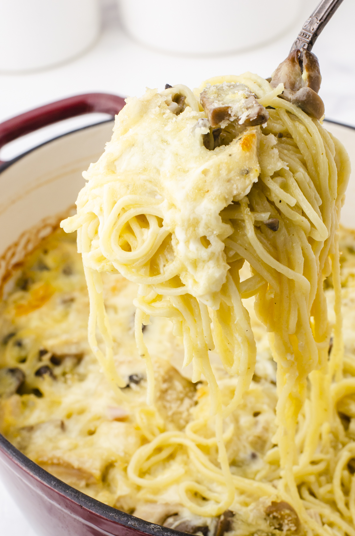 Turkey tetrazzini recipe being scooped out of a large dutch oven with the noodles dripping off the spoon.