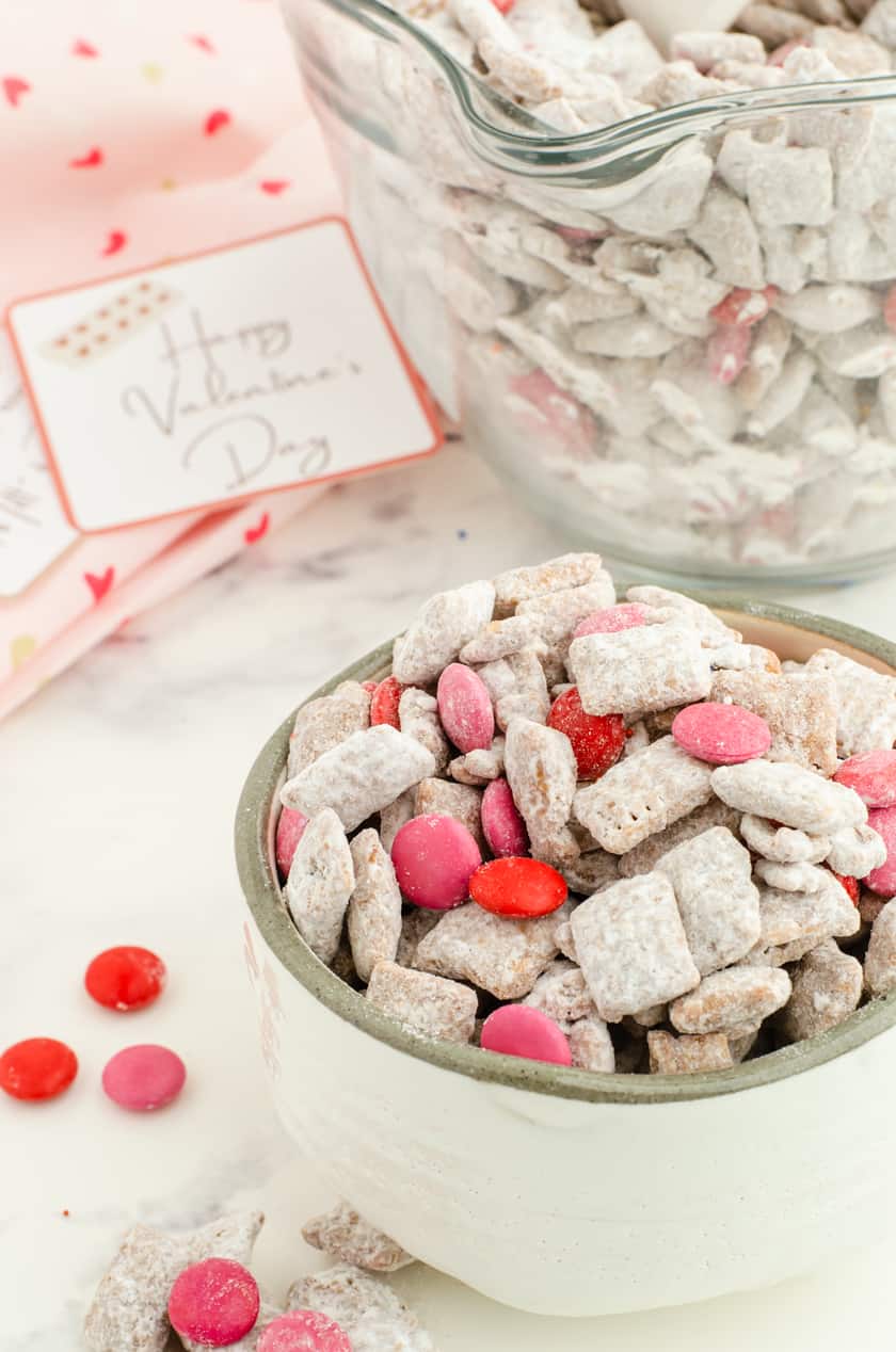 a bowl of valentines puppy chow mix with a valentines card behind it