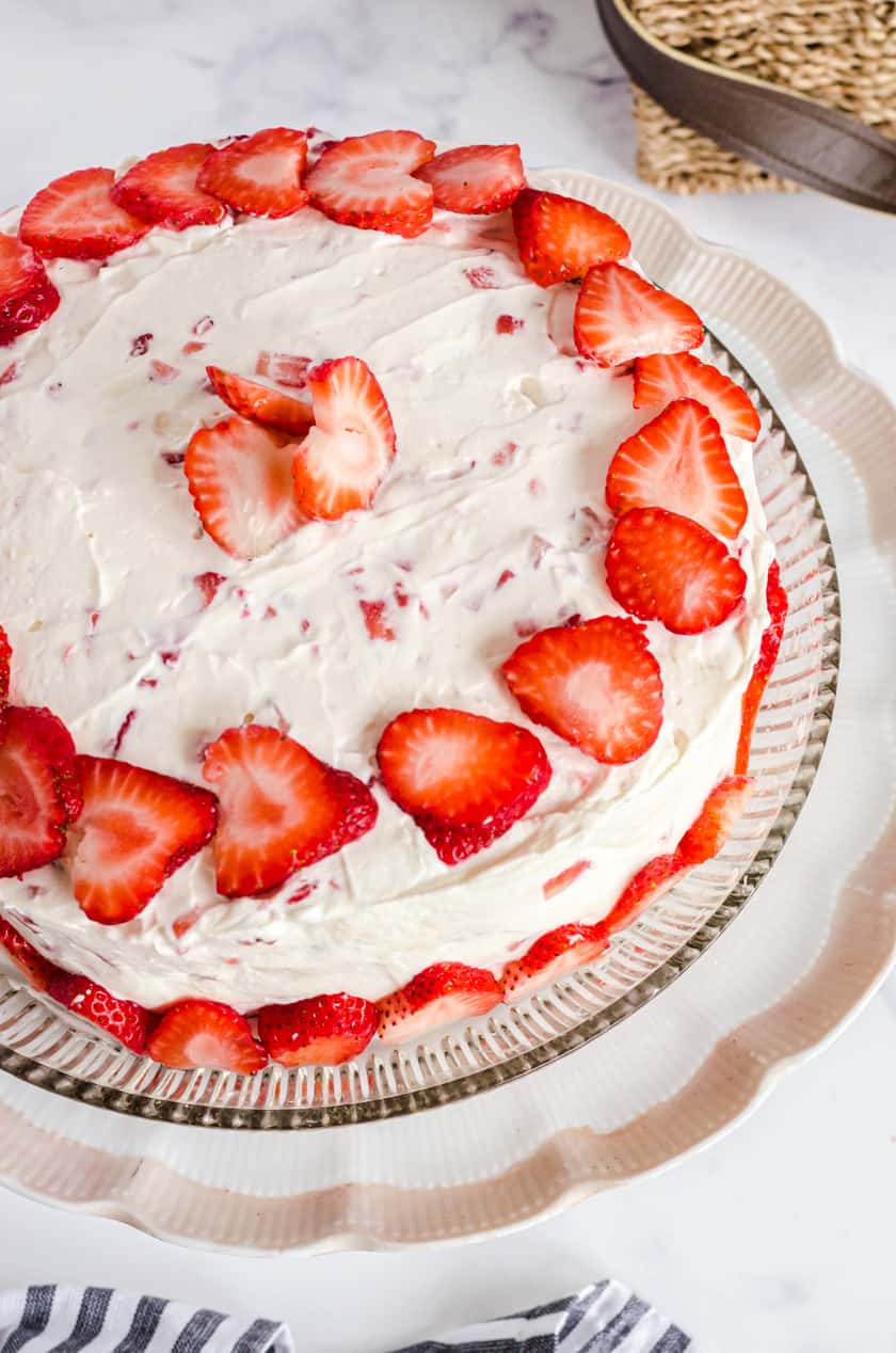 A vanilla strawberry cake with fresh strawberry icing on a cake platter.